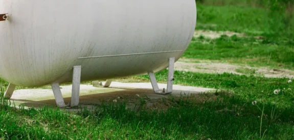 A large white propane tank, installed with a focus on propane safety, stands on a concrete pad surrounded by green grass in an outdoor area on a sunny day.