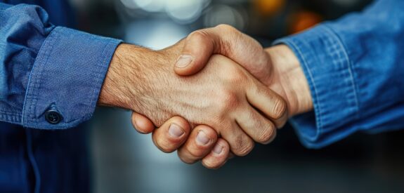 Two people in blue long-sleeved shirts are shaking hands, suggesting agreement or partnership, with a blurred background—perfect for capturing an authentic moment in a short-form video.
