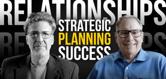 Two men pose before a backdrop reading RELATIONSHIPS, STRATEGIC PLANNING, SUCCESS; one in a blazer, one in a blue polo.