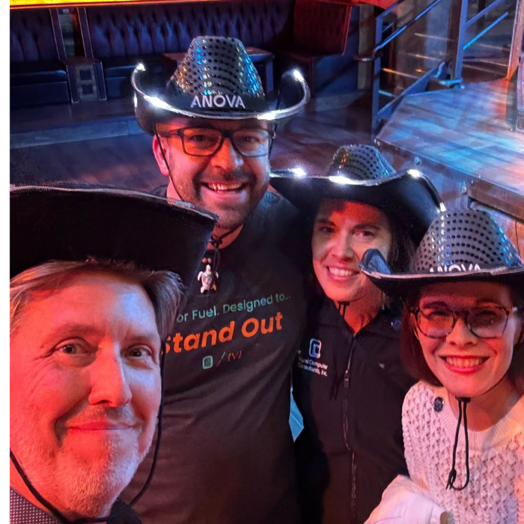 Four people in LED-lit black cowboy hats smile indoors in a dim room with wooden floors and booths.